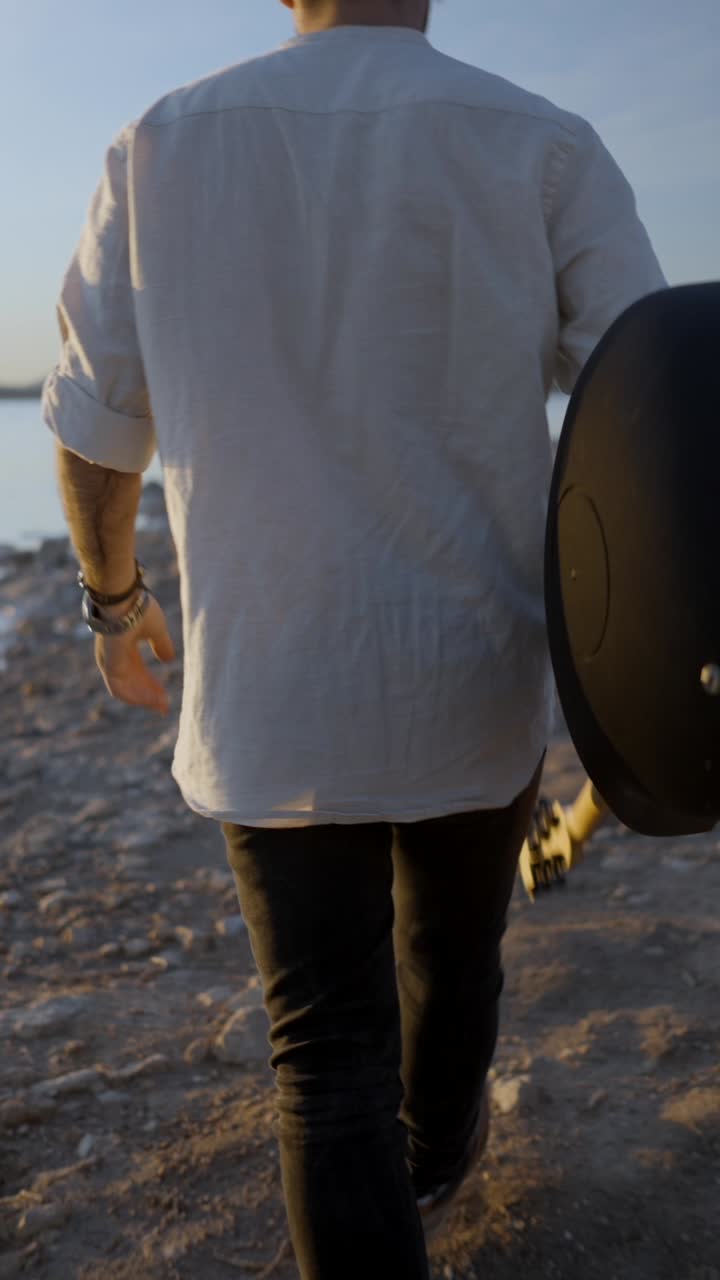 Man Walking with Guitar by the Water at Sunset