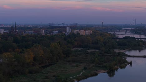 warsaw poland in autumn twilight, aerial view of national football stadium, vistula river bridges and coal power plant in misty skyline