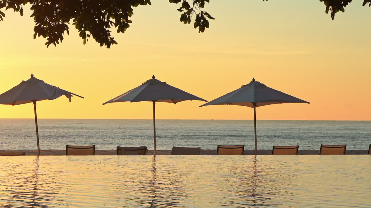 Beautiful golden tropical island sunset in paradise. Infinity pool reflection of setting sun and colors of evening sky on ripples in calm water. Peaceful scene of luxury resort in the evening