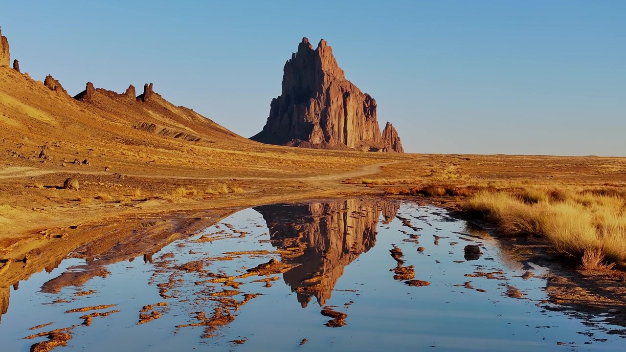 L'acqua calma riflette Shiprock mentre il drone sale lentamente, creando una composizione desertica specchiata con un leggero movimento.