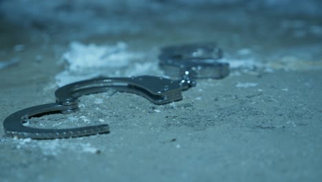 handcuffs lay on dusty floor in torture room lighted with a flashlight