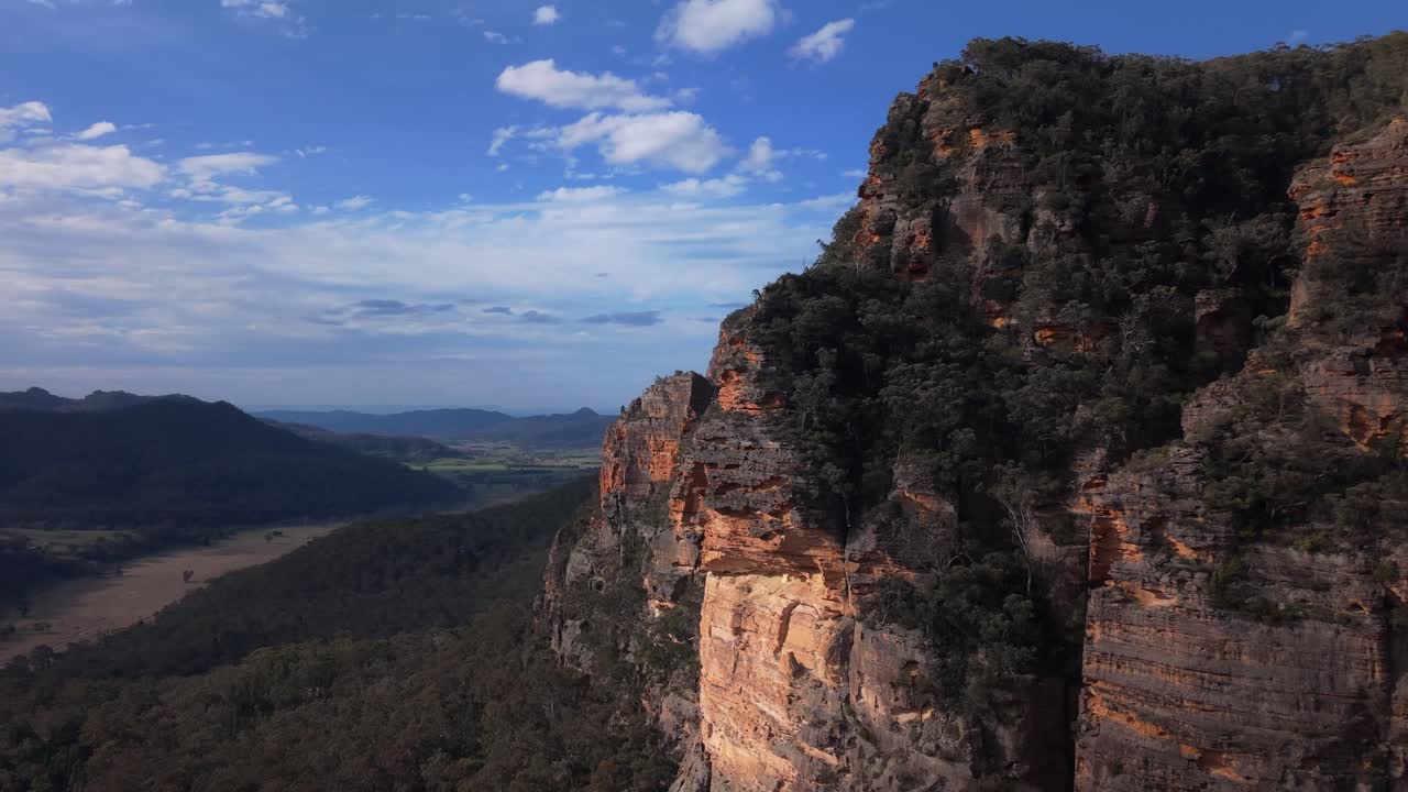 Ripresa ravvicinata con drone di ripide scogliere di arenaria con una fitta foresta sottostante e orizzonte aperto sullo sfondo, Blue Mountains, Nuovo Galles del Sud, Australia