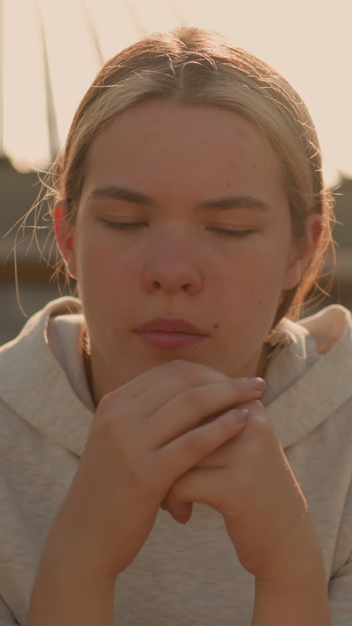 primer plano de una mujer contemplativa sentada en las gradas rústicas del estadio, las manos unidas cerca de su cara, parece reflexiva, con una expresión suave contra un fondo borroso