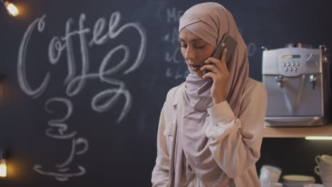 mujer musulmana hablando por teléfono en una cafetería