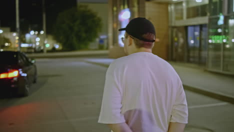 man walking at night on a city street, near a black car