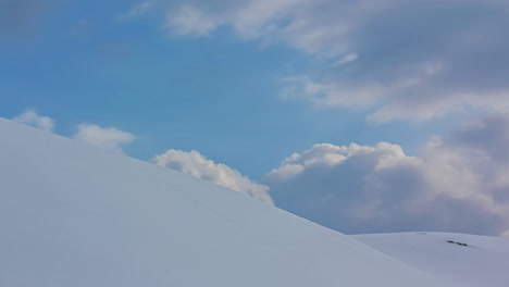 clouds move over round snowy hills with foot tracks, static timelapse