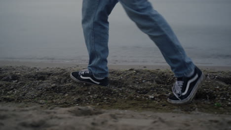 casual sneakers walking on sea shore closeup. man feet enjoying walk on beach