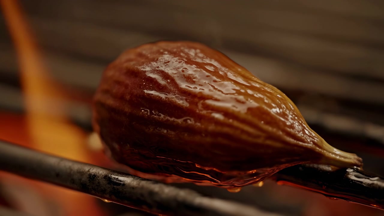 Tight close-up of a single roasted chestnut resting on a metal grill above glowing charcoal embers. The glossy cracked brown shell catches warm ember light