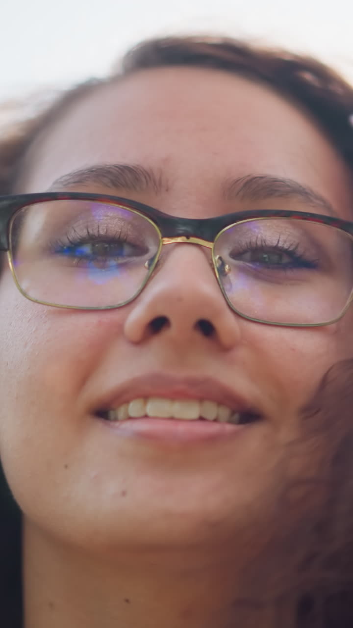 primer plano de una joven con gafas ajustando su cabello mientras posa y sonríe cálidamente frente a la cámara, la luz natural suave crea un brillo suave alrededor de su cara