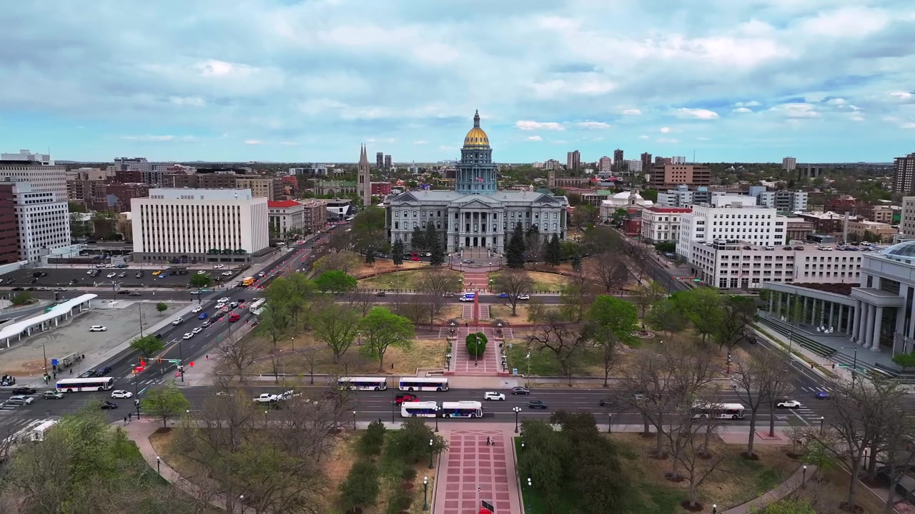 Luftfoto med drone af Denver bylandskab: Civic Center Park eventcenter, downtown Lodo, Capitol Hill og Colorado Capitol-bygningerne. Forårseftermiddag med overskyet blå himmel, tosporet vej med biler og trafik i fremadgående bevægelse.