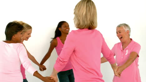 mujeres bailando en círculo y tomadas de la mano usando rosa para el cáncer de mama