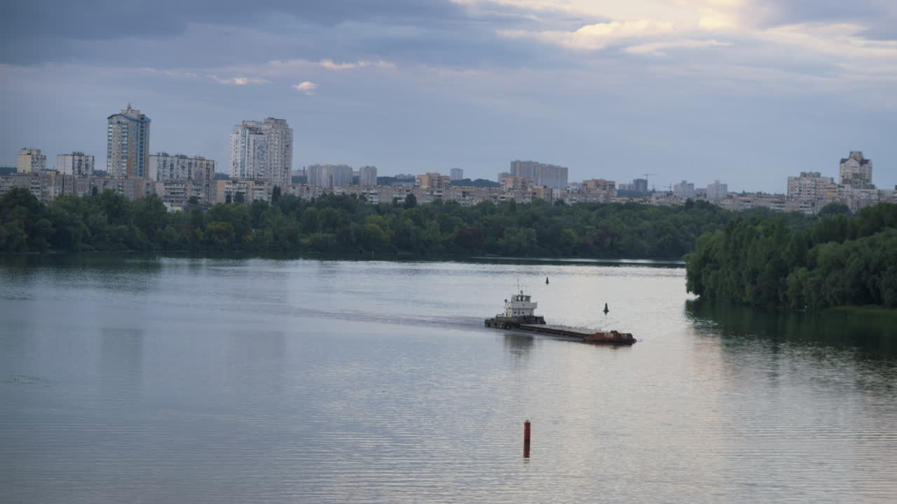 드론은 저녁에 흐르는 강에서 도시 풍경을 촬영했다. 견인 보트가  ⁇ 은 빈 배를 밀고