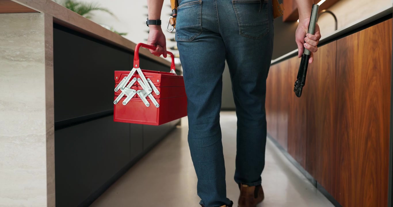 Tuttofare che trasporta una cassetta degli attrezzi rossa e un attrezzo in una cucina moderna