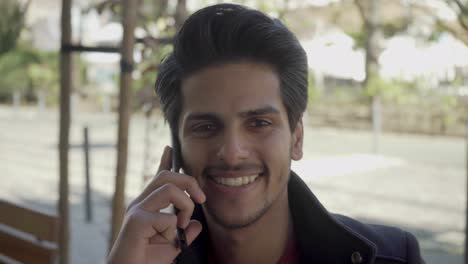 Young-man-talking-by-cell-phone-and-smiling-at-camera