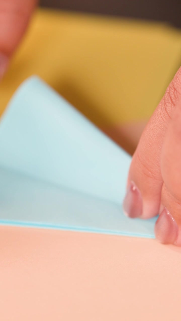 Close-up shot of fingers precisely folding blue paper on a colorful surface for origami