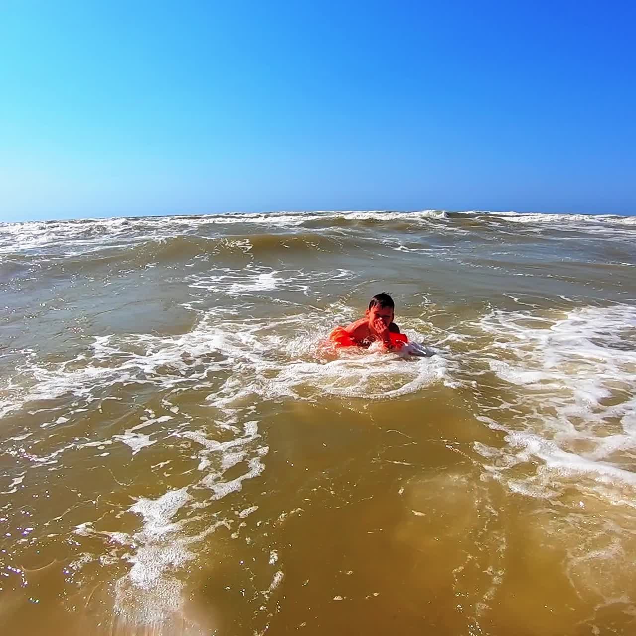 Boy enjoys in waves in the sea. Cute child jumping into big waves with white foam in a sunny summer day. Happy childhood.