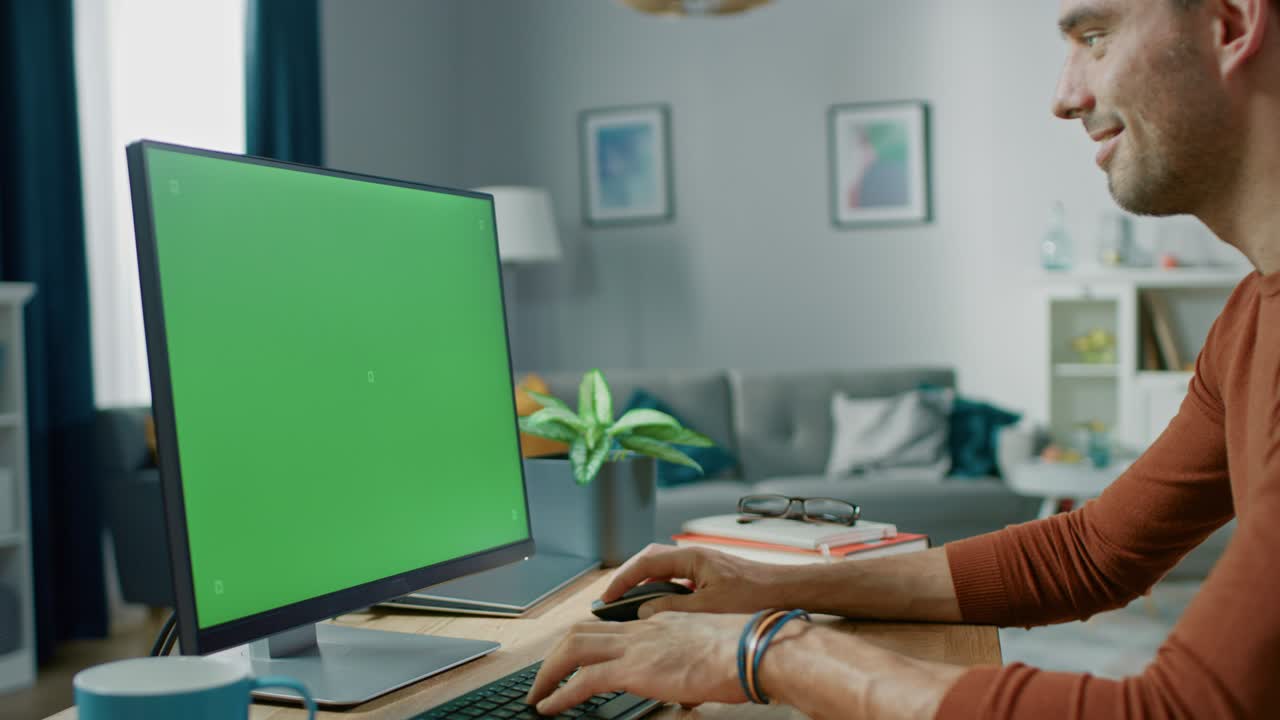 un hombre guapo sentado en su escritorio en casa usa una computadora personal con una pantalla clave de croma.