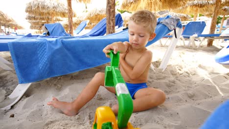 Un-Niño-Sentado-En-La-Arena-Juega-Solo-Con-Un-Raspador-De-Plástico,-Durante-El-Día