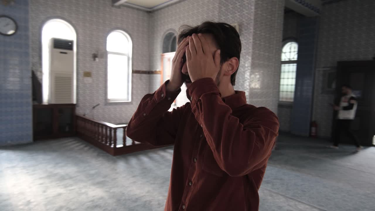 A young bearded man standing inside a mosque praying to god, Muslims who go to historical and holy places pray