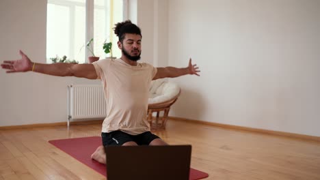 bearded sporty male breathing deeply, sitting with closed eyes on exercise mat in living room