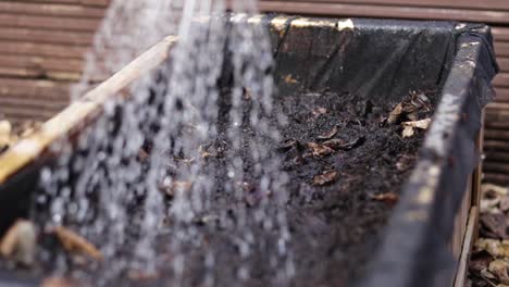 a wooden container with compost in, being watered with a watering can