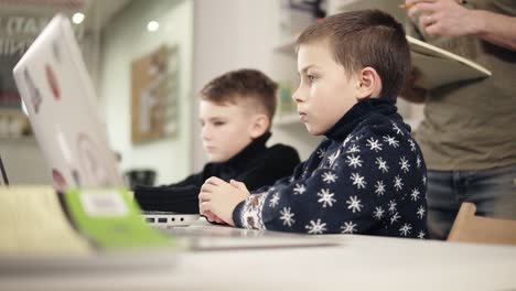 Footage-of-two-little-boys-sitting-in-front-of-their-laptops-and-male-unrecognizable-figure-standing-beside-them.