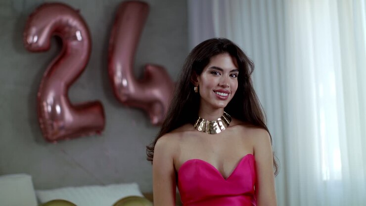 Una modella in un bellissimo vestito rosso con gioielli d'oro sta in piedi con un grande sorriso.