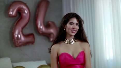 a fashion model in a beautiful red dress with gold jewelry stands with a big smile