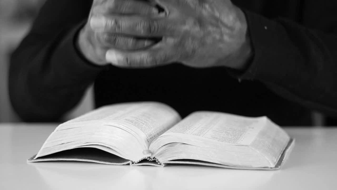 Hands clasped in prayer over an open Bible