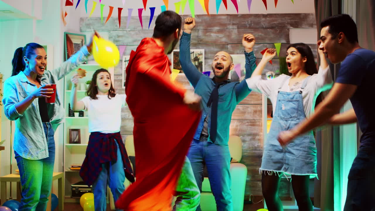 joven emocionado con una capa roja de superhéroe en la fiesta con sus amigos