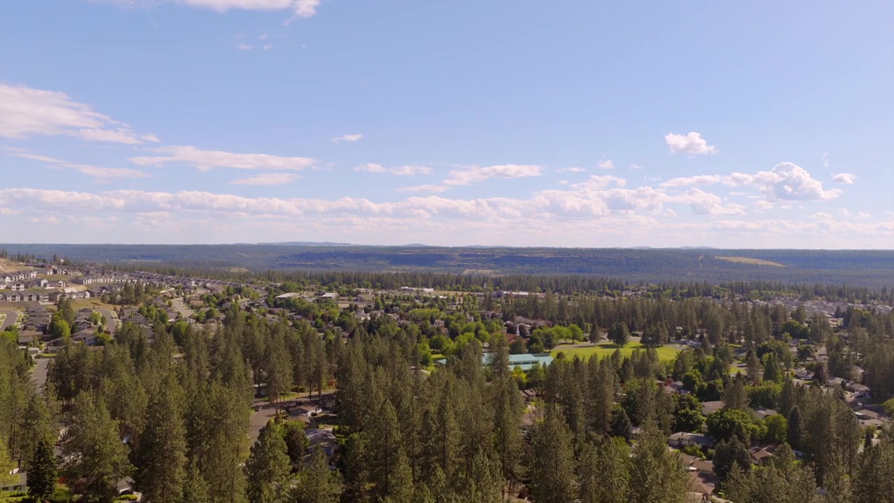 Vista aerea da un quartiere collinare a Spokane, Washington, con grandi case in primo piano e una valle boscosa che si estende fino all'orizzonte.
