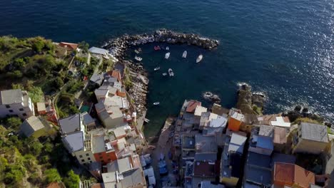 Town-of-Riomaggiore-in-the-Cinque-Terre-Italy-with-buildings-and-boats-near-the-sea,-Aerial-lowering-reveal-shot