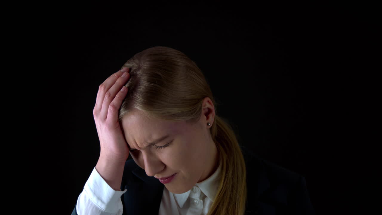 Slow motion shot of pretty woman with headache in studio with black background,slow motion