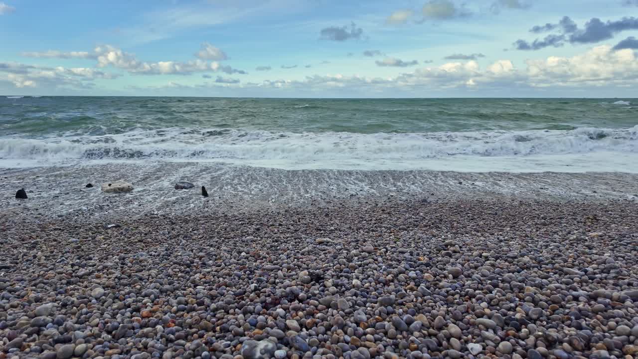Havbølger når stenstrand under en overskyet himmel, Etretat, Normandiet i Frankrig.