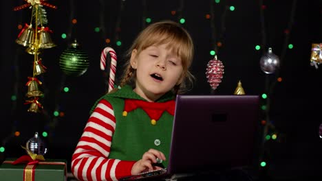 Kid-girl-in-Christmas-elf-costume-doing-shopping-online-using-laptop,-browsing-on-social-media