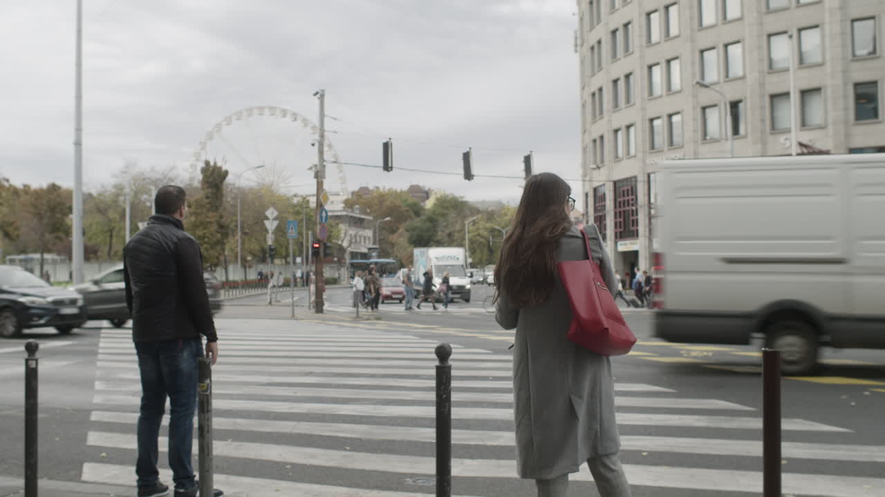A young woman and man at a crosswalk waiting to cross Bajcsy Zsilinszky road in the city of Budapest.