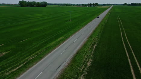 car-driving-alone-in-the-middle-of-green-fields,-aerial-tilting-down