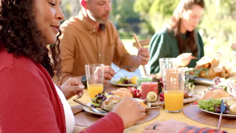 happy diverse male and female friends eating thanksgiving celebration meal in sunny garden