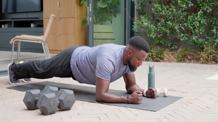 Man holding plank lowering resting wiping sweat returning on patio near weights for fitness