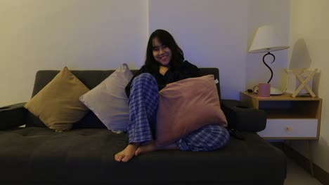 A-happy,-Asian-girl-sitting-on-the-couch,-watching-TV-while-smiling-and-laughing