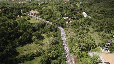 una imagen aérea de una carretera llena de gente en bali y un sacerdote caminando por la calle con ropa tradicional para una ceremonia hindú en la isla