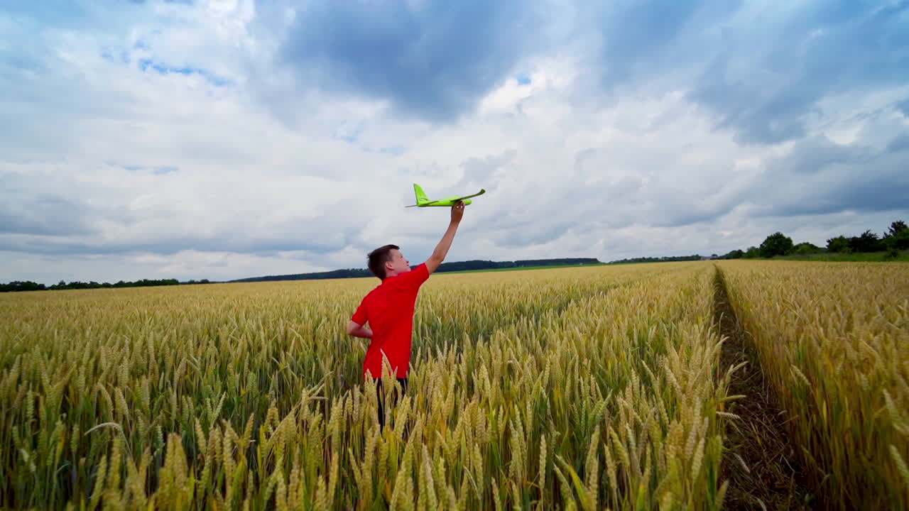 Happy boy runs on field. Boy in a red t-shirt launches toy plane in agricultural land. Summer vacation outdoors. Slow motion.