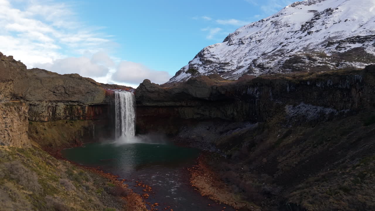 Forward right orbit reveals Salto del Agrio in Neuquen, Argentina, a plunge waterfall into a turquoise pool, ringed by basalt cliffs and snowy Andes