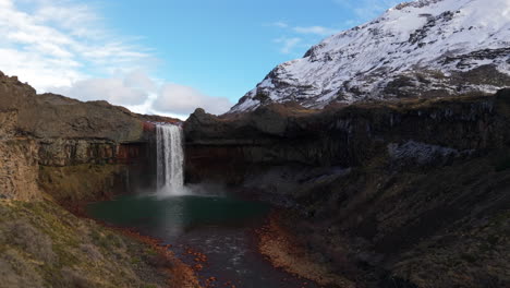 forward right orbit reveals salto del agrio in neuquen, argentina, a plunge waterfall into a turquoise pool, ringed by basalt cliffs and snowy andes