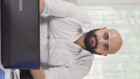 Vertical-video-of-Home-office-worker-man-looking-dull-at-camera.