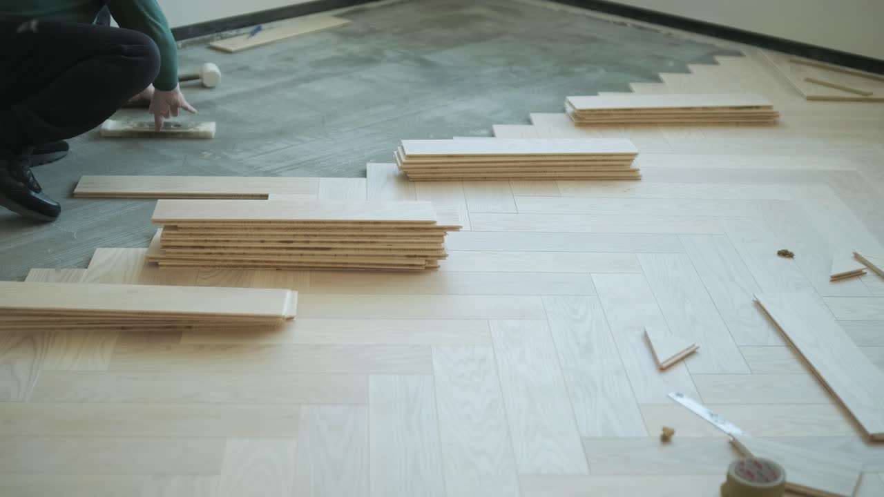 Worker installing wooden flooring with hammer and tapping block
