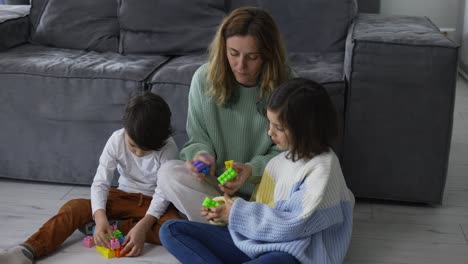 Happy-young-adult-mother-playing-with-two-cute-small-kids,-having-fun-sit-on-floor