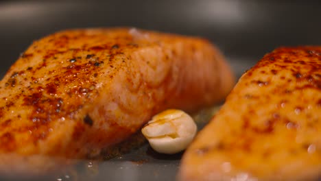 close up of salmon fish fillets gently cooking in butter and garlic seasoned with salt and pepper 4k