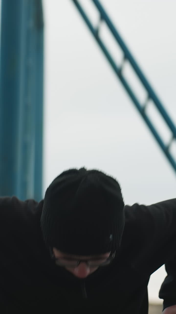 Close-up of a young boy working out on a metal bar, dressed in a black outfit and glasses