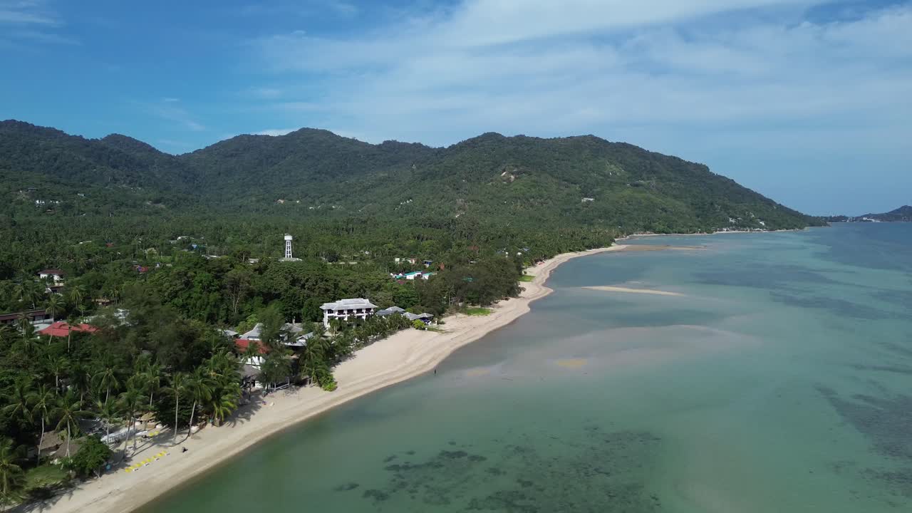 Scenic aerial view of Koh Phangan island showing coastline, sandy beach, lush palm trees and seaside bungalows in tropical Thailand captured by drone on a sunny day